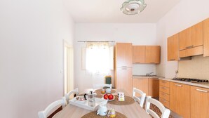 A dining area with a wooden table, white chairs, and a kitchen with wooden cabinets and a stove. - Cascina Mimì by BarbarHouse (Nardò)