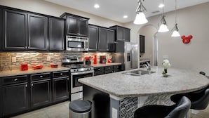 A modern kitchen with dark cabinets, stainless steel appliances, a granite countertop, and pendant lighting. - Last Minute Disney! Private Pool, Hot Tub & Themed Bedrooms. Book Now! #65531 (Orlando)
