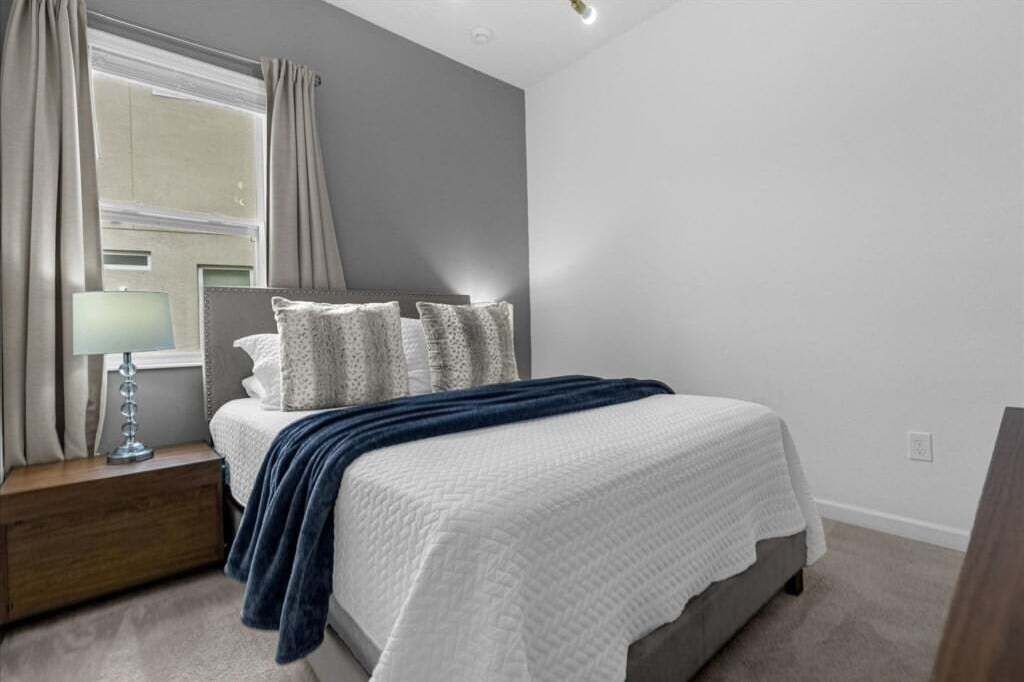 A bedroom with a bed, a nightstand, a lamp, and a window with curtains.