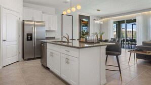 Una cocina moderna con gabinetes blancos, un refrigerador de acero inoxidable y una isla central con taburetes de bar.