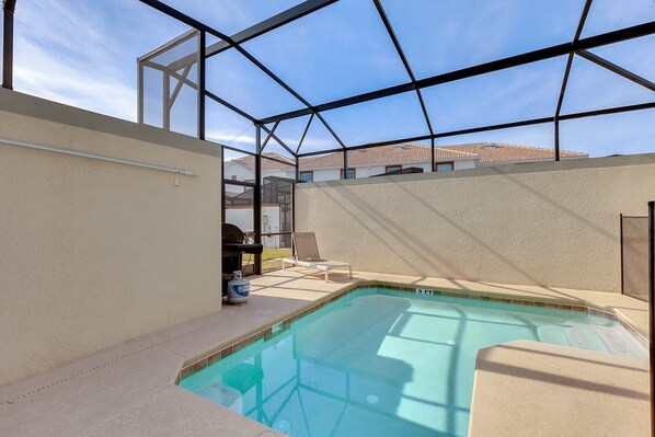 A swimming pool with a glass enclosure, a lounge chair, and a small table with a water bottle. - Last Minute Disney Getaway! Private Pool & Themed Bedrooms. Book Now! #65583 (Orlando)