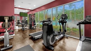A gym with cardio machines, weight machines, and a large window offering a view of greenery. - Last Minute Disney Getaway! Townhouse with Private Pool. Book Now! #65649 (Orlando)