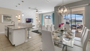 Una cocina moderna con una isla central, comedor con sillas blancas y vistas al exterior.