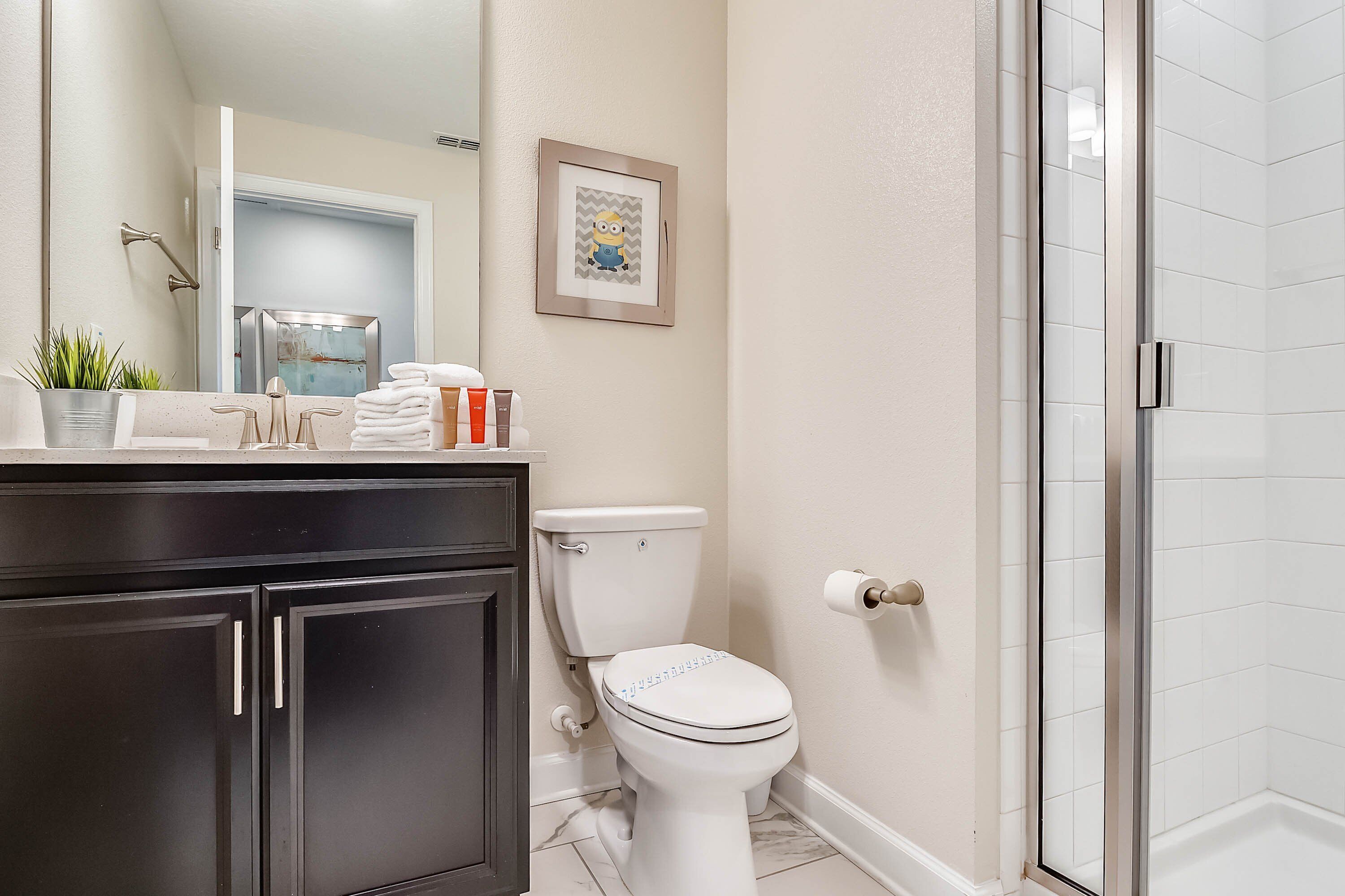 Une salle de bain comprenant des toilettes, un lavabo avec un miroir, une douche et un tableau encadré au mur.