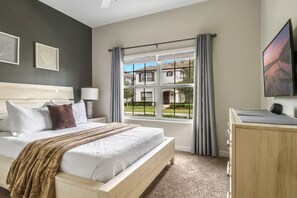 A bedroom with a bed, a desk, a TV, and a window with curtains.