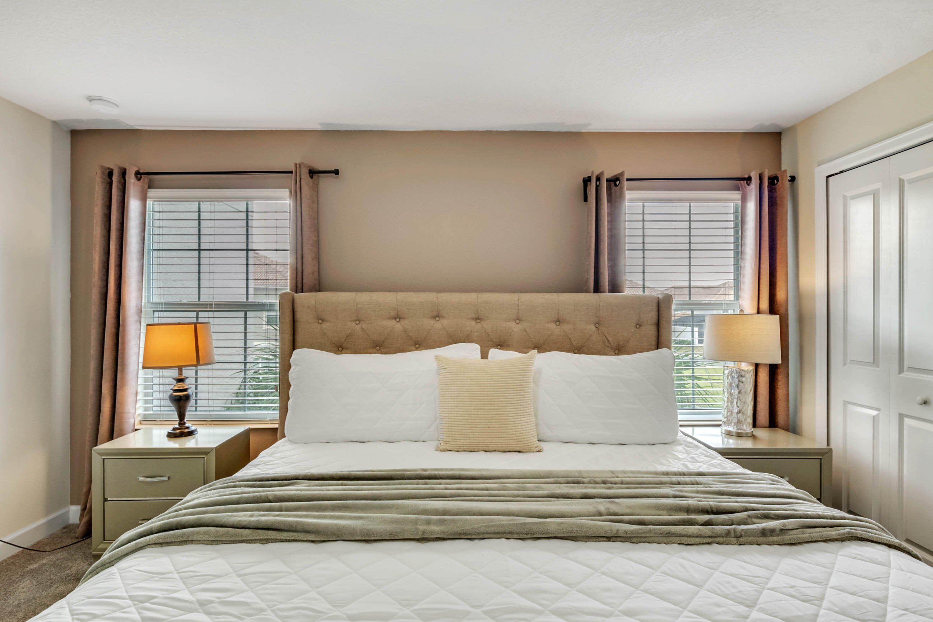 A neatly arranged bedroom with a large bed, two bedside tables with lamps, and a window with curtains.