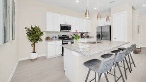 A modern kitchen with white cabinets, stainless steel appliances, a granite island, and bar stools. - 5 BD/5BA Themed House Near Disney (Kissimmee)