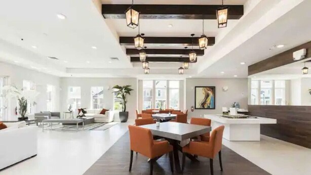 A spacious, modern hotel lobby with a central dining area, large windows, and contemporary lighting fixtures. - 5 BD/5BA Themed House Near Disney (Kissimmee)