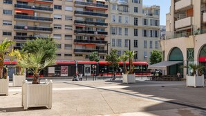 A multi-story residential building with balconies, a bus stop, and outdoor seating area. - Happyfew Palais des arts (Nice)