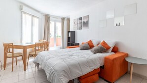 A modern bedroom with a bed, orange sofa, and a dining area with a table and chairs. - Happyfew Palais des arts (Nice)
