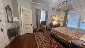 A bedroom with a four-poster bed, a television, a desk with a chair, and a red patterned rug.