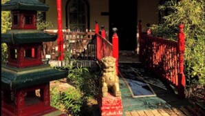 A traditional building with a red roof and a stone lion statue in front.