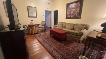 A living room with a sofa, a red ottoman, a television, and a patterned rug.