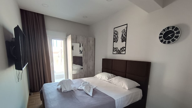 Un lit bien fait, avec du linge de lit blanc, une tête de lit marron et une horloge murale.