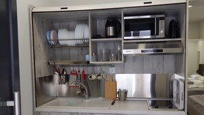 Une cuisine compacte dotée d’un four à micro-ondes encastré, d’un évier et de placards de rangement.