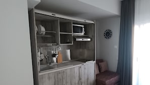Une cuisine compacte dotée d’appareils électroménagers intégrés, d’un meuble en bois et d’un petit coin salon avec un canapé et des rideaux.