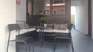 Un coin repas comprenant une table ronde et quatre chaises, un banc agrémenté de coussins à motifs et une plante en pot.