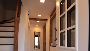 A hallway with a wooden staircase on the left, a white door with glass panels on the right, and a tiled floor.