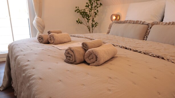 A neatly made bed with rolled towels, a bedside plant, and a lamp.