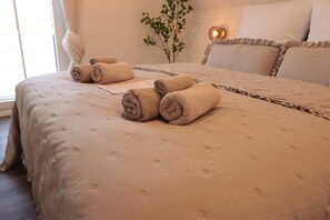 A neatly made bed with rolled towels, a bedside plant, and a lamp.