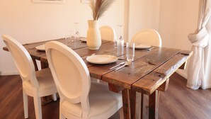 A dining table set with white chairs, a vase with pampas grass, and wine glasses.