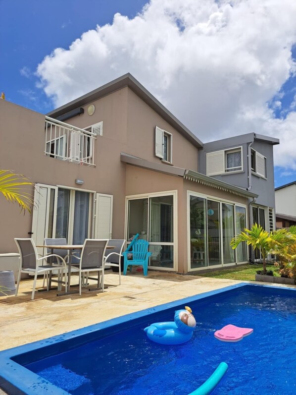 A two-story house with a swimming pool, outdoor furniture, and a balcony.