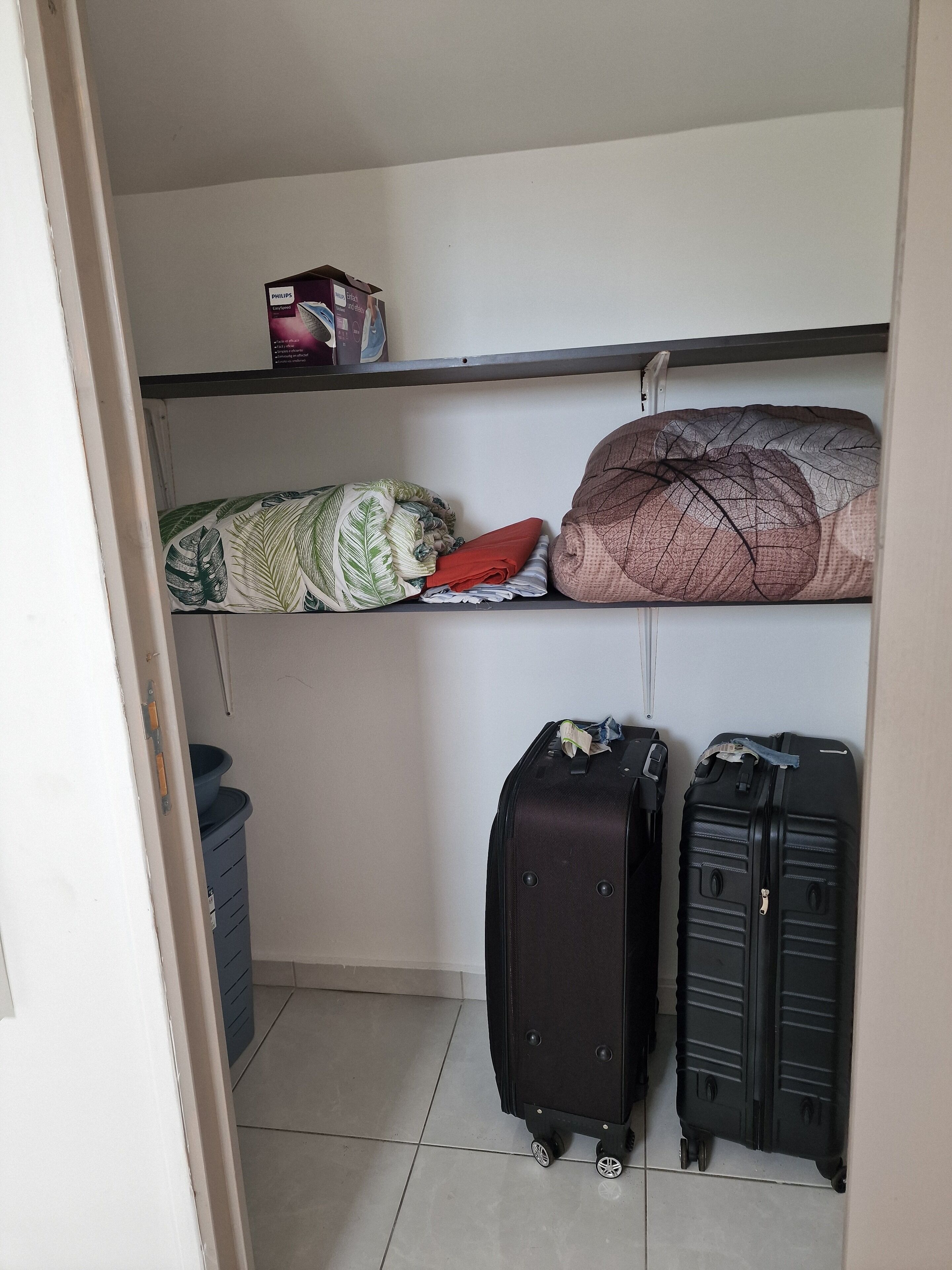 A storage closet with shelves holding folded blankets and a trash bin.