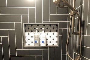 Un espace douche dotĂ© dâune Ă©tagĂšre intĂ©grĂ©e oĂč sont rangĂ©s deux flacons de shampoing et dâaprĂšs-shampoing.