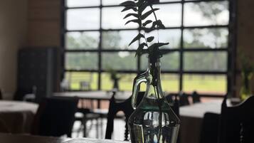 A clear glass vase with a plant on a wooden table in a room with large windows.