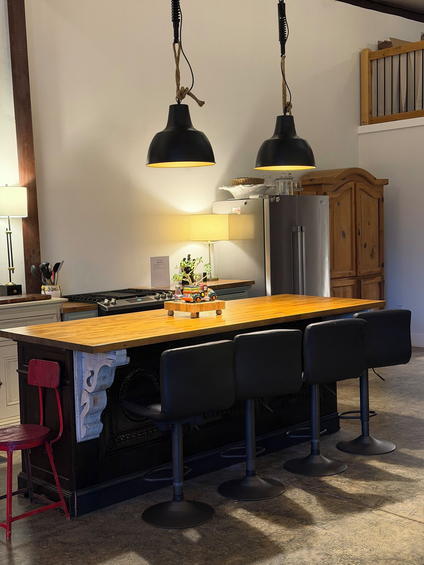 A kitchen with a central island, bar stools, a refrigerator, and hanging pendant lights.