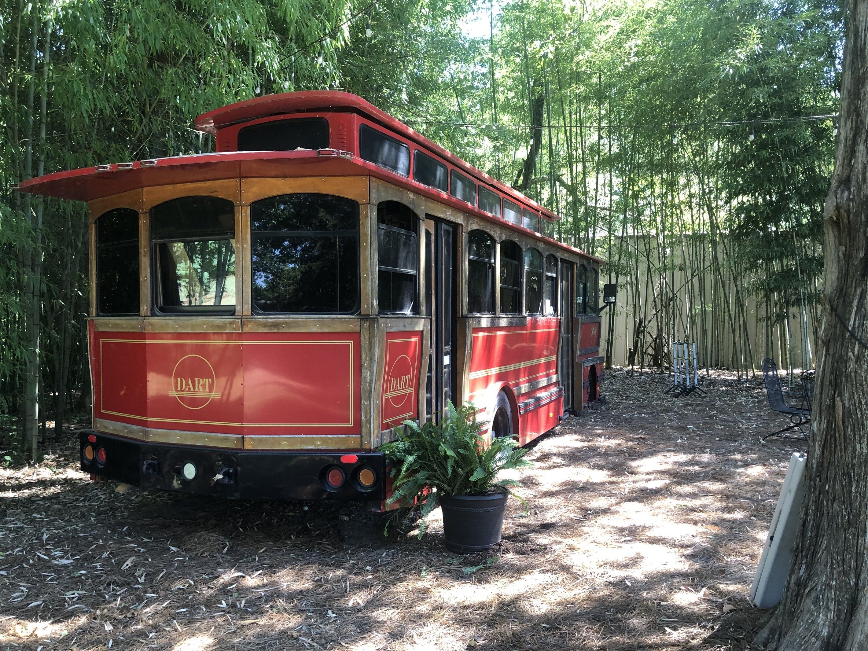 Ein alter, roter Doppeldeckerbus steht in einem bewaldeten Gebiet, in der Nähe befindet sich ein Blumentopf.