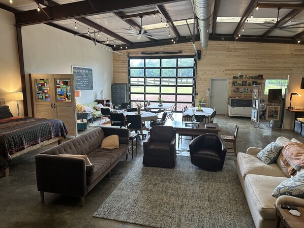 A spacious room with a large window, a sofa, a dining table, and a kitchen area. - The Studio at Green Pastures - Sheep Farm (Montevallo)