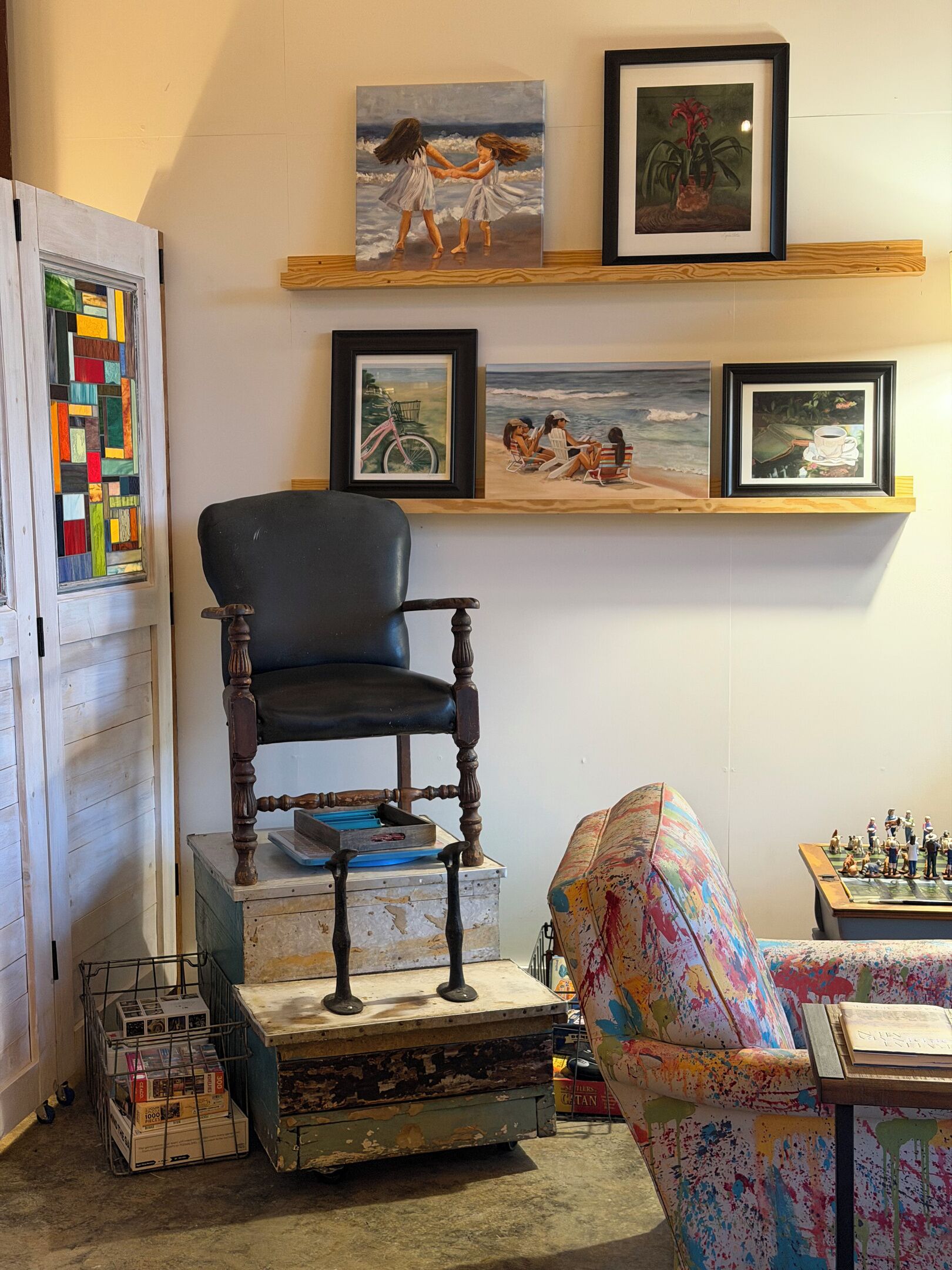 A room with a wooden chair, a colorful armchair, a shelf with framed artwork, and a vintage bicycle.