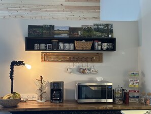 Una cocina con cafetera, microondas y repisas con tazas y una cesta.