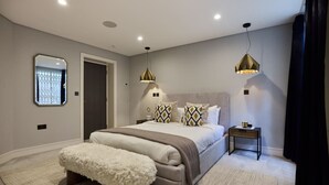 Une chambre à coucher moderne avec un grand lit, deux lampes de chevet, une table de chevet et un banc blanc moelleux.