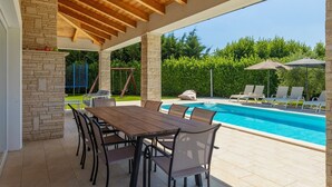 Eine Außenpatio mit Pool, Steinpfeilern, Holzbalken und Gartenmöbeln.