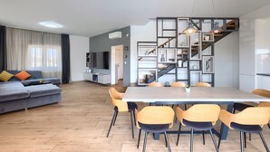 Ein modernes Wohnzimmer mit grauem Sofa, einem Esstisch mit Stühlen und einer Treppe mit integriertem Bücherregal.
