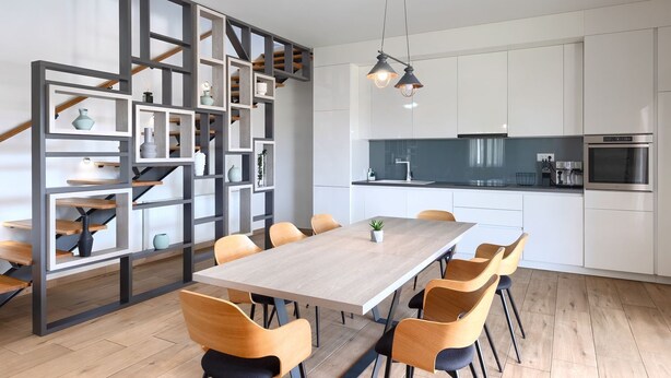Eine moderne Küche mit weißen Schränken, einem eingebauten Backofen und einem Essbereich mit einem Holztisch und Stühlen.