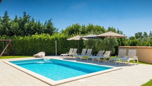 Ein rechteckiger Pool mit einer gefliesten Liegefläche, umgeben von Liegestühlen und Sonnenschirmen.