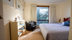 Een slaapkamer met een bed, een bureau met stoel, een boekenkast en een raam met gordijnen.