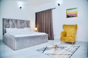 A bedroom with a bed, a yellow armchair, a painting, and a curtain. - Oasis Villa-Lekki (Lekki)