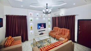 Ein Wohnzimmer mit einer Sofagarnitur, einem Couchtisch, einem Fernseher und dekorativen Regalen.