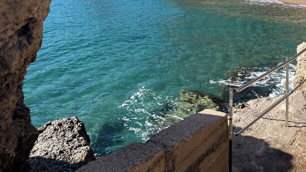 Paisaje costero con aguas turquesas cristalinas, acantilados rocosos y una playa arenosa.