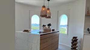 Una cocina moderna con una isla de mármol, armarios de madera y dos ventanas amplias con vistas al campo.