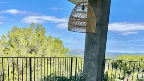Un balcón con mobiliario de mimbre, una lámpara colgante y vistas a la vegetación y montañas.