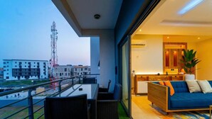 A balcony with a dining table and chairs, a sofa, and a view of buildings and a communication tower. - Premium Luxury Apartment by Smart Home  (Lekki)