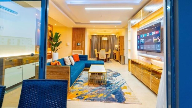 A modern living room with a blue sofa, a coffee table, and a TV. - Premium Luxury Apartment by Smart Home  (Lekki)