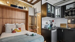 Een compacte slaapkamer met een bed, nachtkastjes en een kleine kitchenette met een gootsteen en kookplaat.