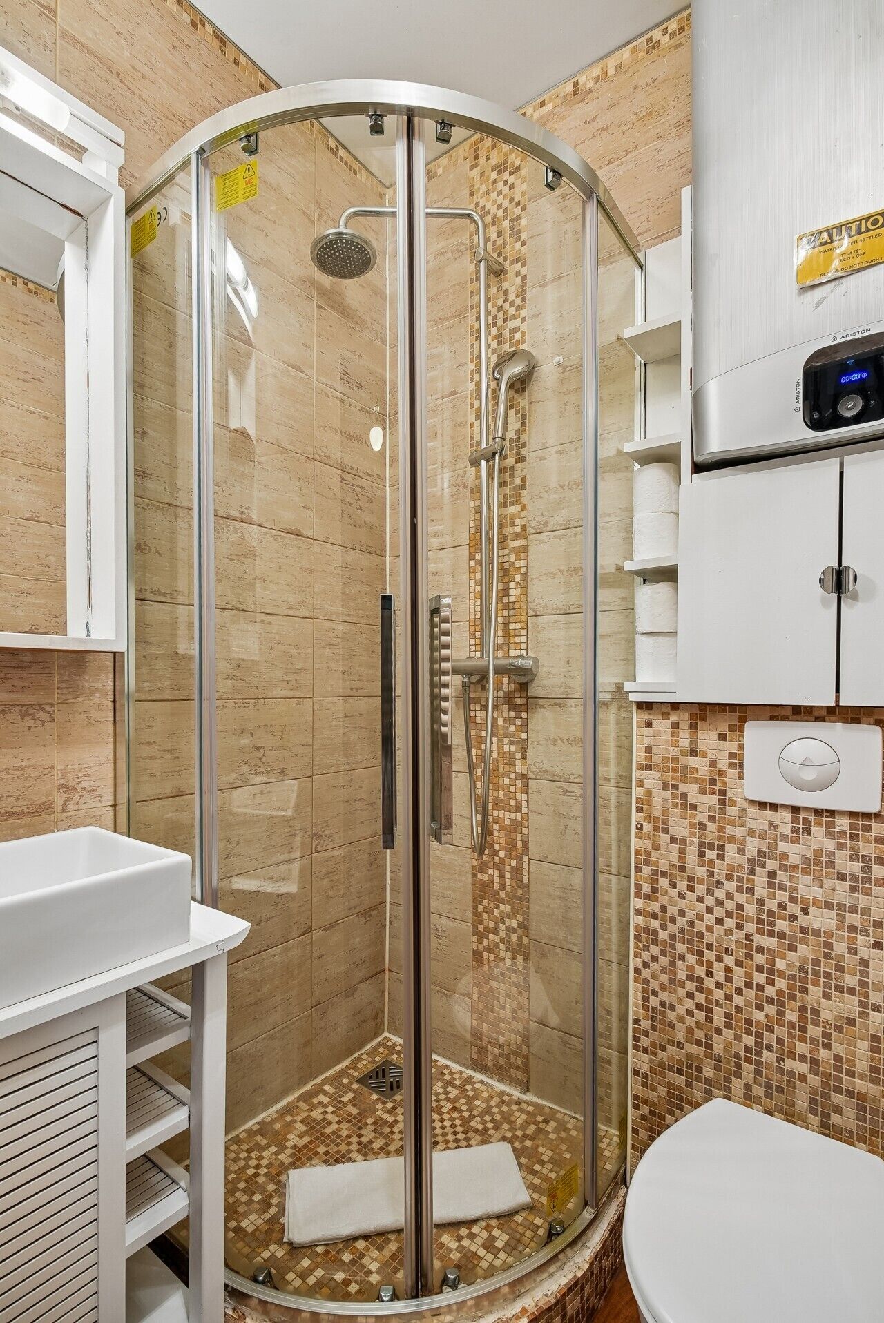 Une cabine de douche fermée par des parois en verre, dotée d’un pommeau de douche à main, d’un lavabo blanc et de toilettes.