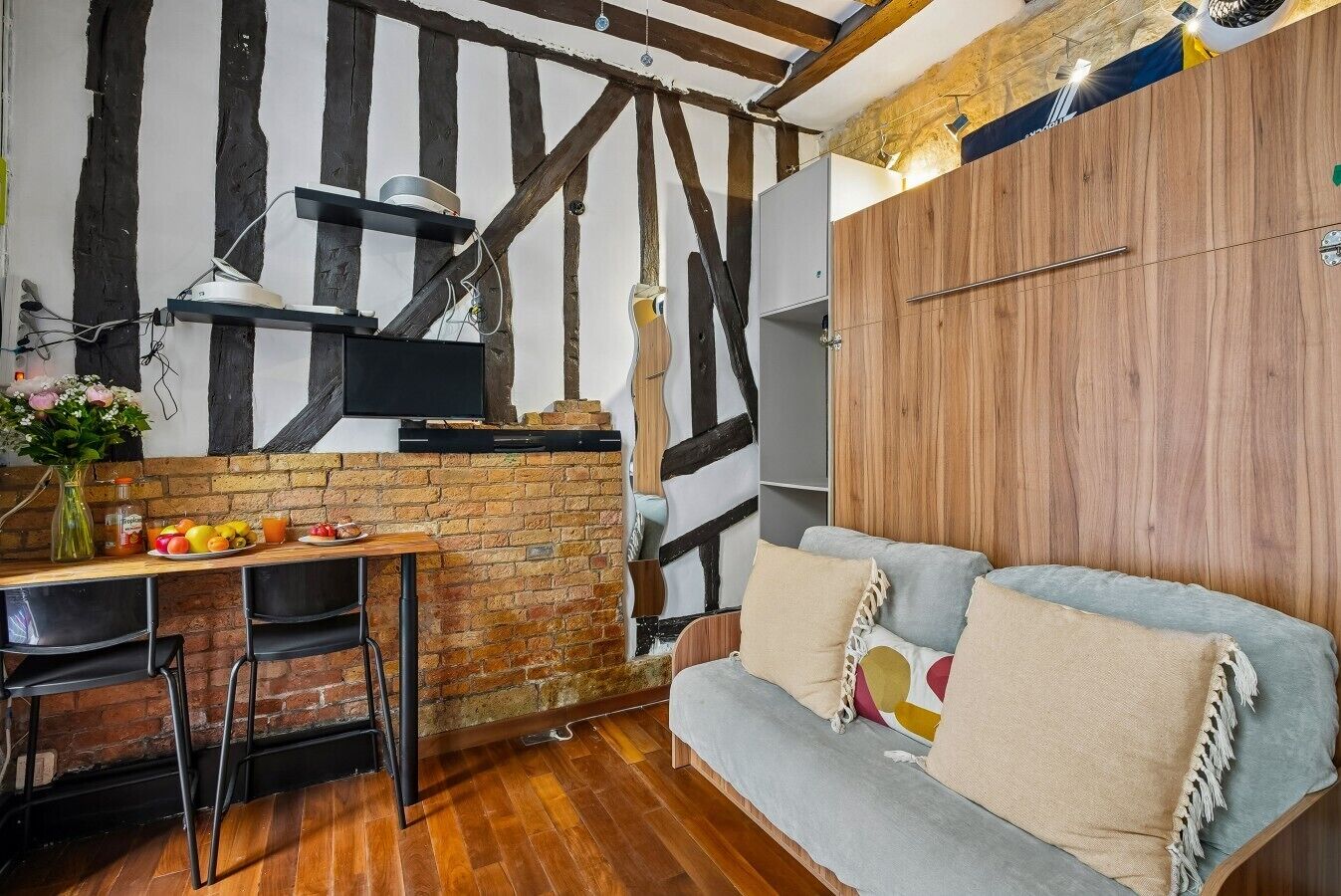Una habitación con paredes de ladrillo visto, techo de madera, un sofá, una mesa con sillas y un televisor.